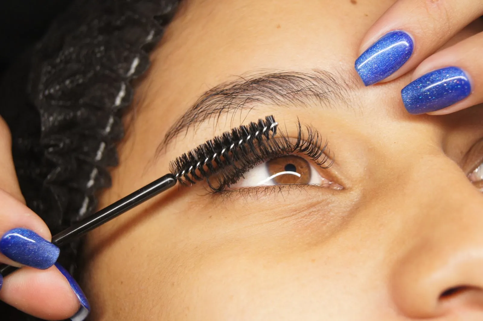 Detailed shot of eyelash extension application on a woman with blue painted nails.
